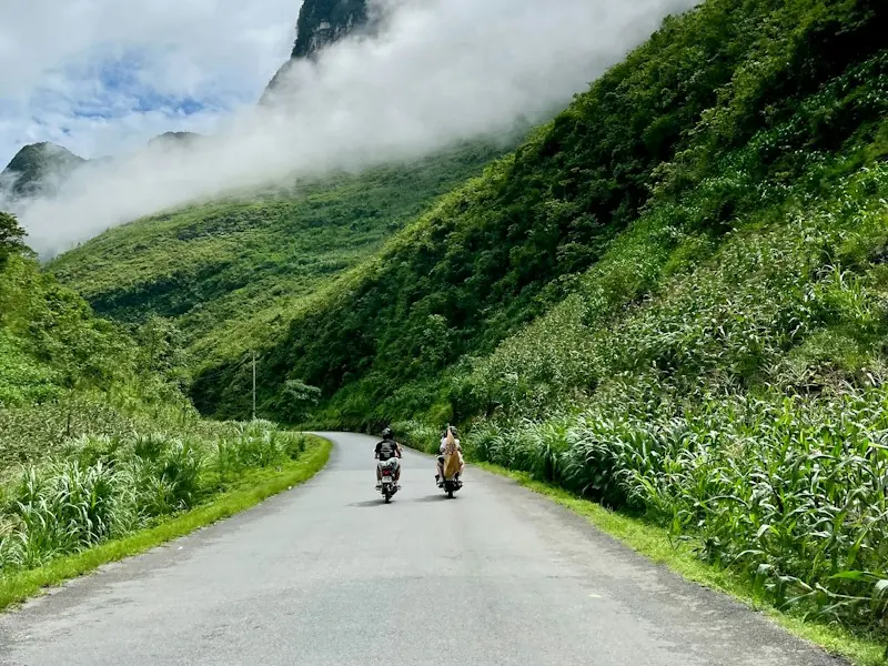 Hai người đi xe máy trên đường đèo giữa núi xanh