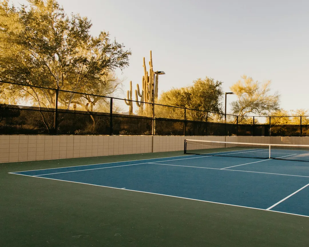 Sân tennis mặt cứng lúc hoàng hôn, có hàng rào và hàng cây phía sau