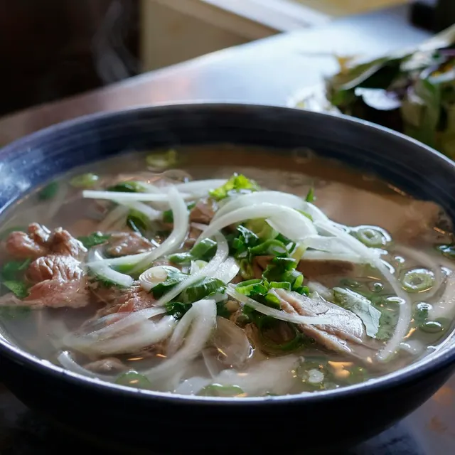 Tô phở bò với thịt bò thái mỏng, hành tây và rau thơm