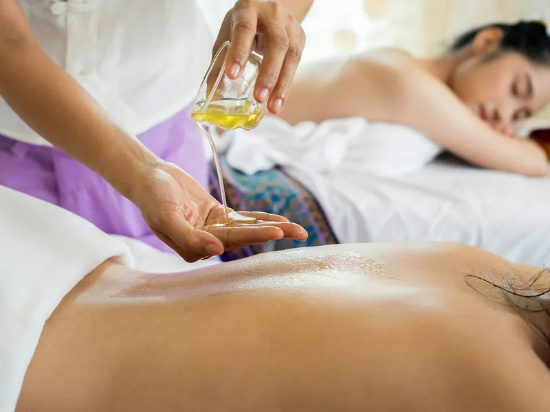 Kỹ thuật viên rót tinh dầu lên lưng khách trong buổi massage