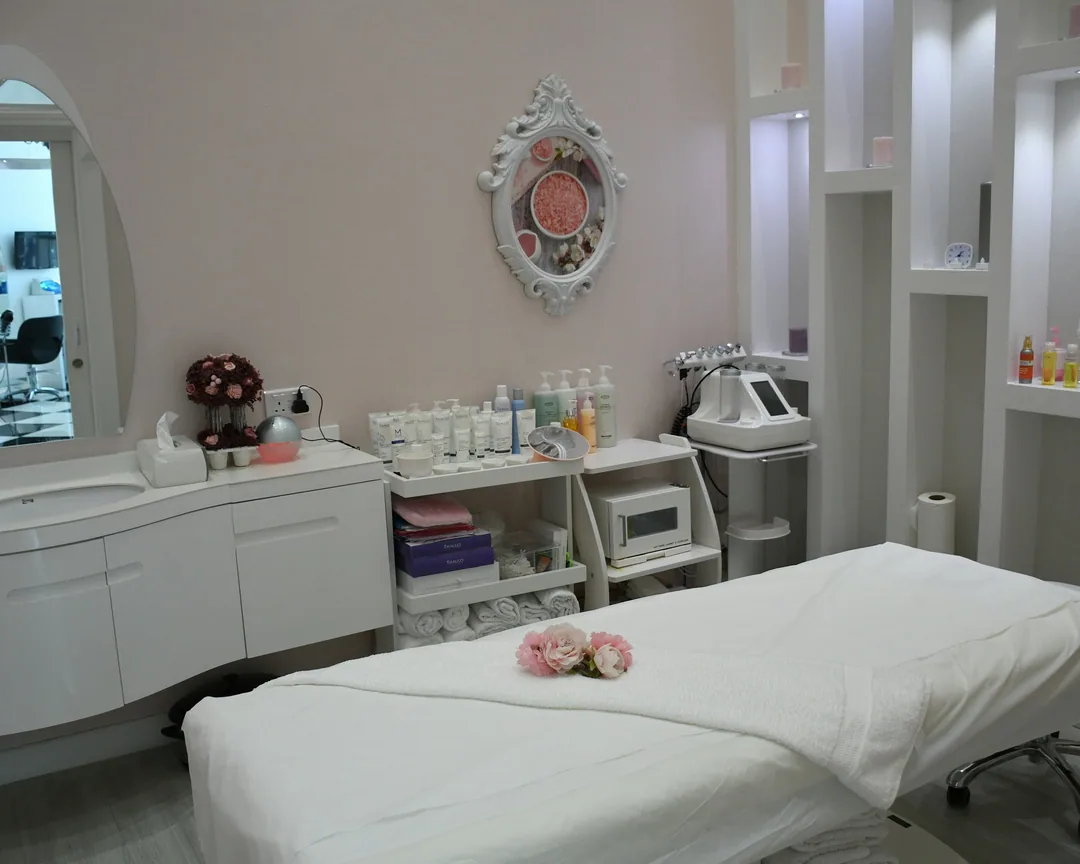 Phòng chăm sóc da tông hồng nude với giường trắng, hoa và kệ mỹ phẩm
